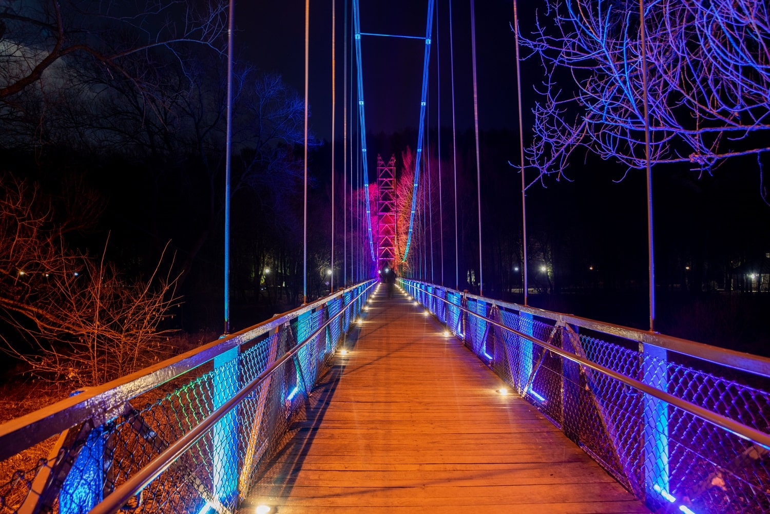 Iluminacje obiektów inżynieryjnych. Widok na most oświetlony na fioletowo i różowo
