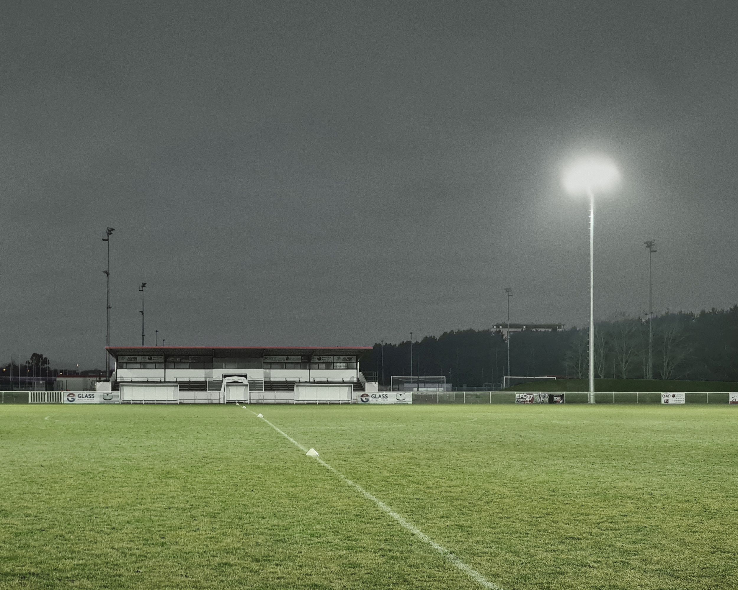 Płyta boiska piłkarskiego o zmierzchu, oświetlona grupą naświetlaczy umieszczonych na wysokim maszcie.